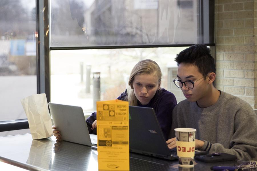 两名学生在大学中心的窗户旁用笔记本电脑工作.