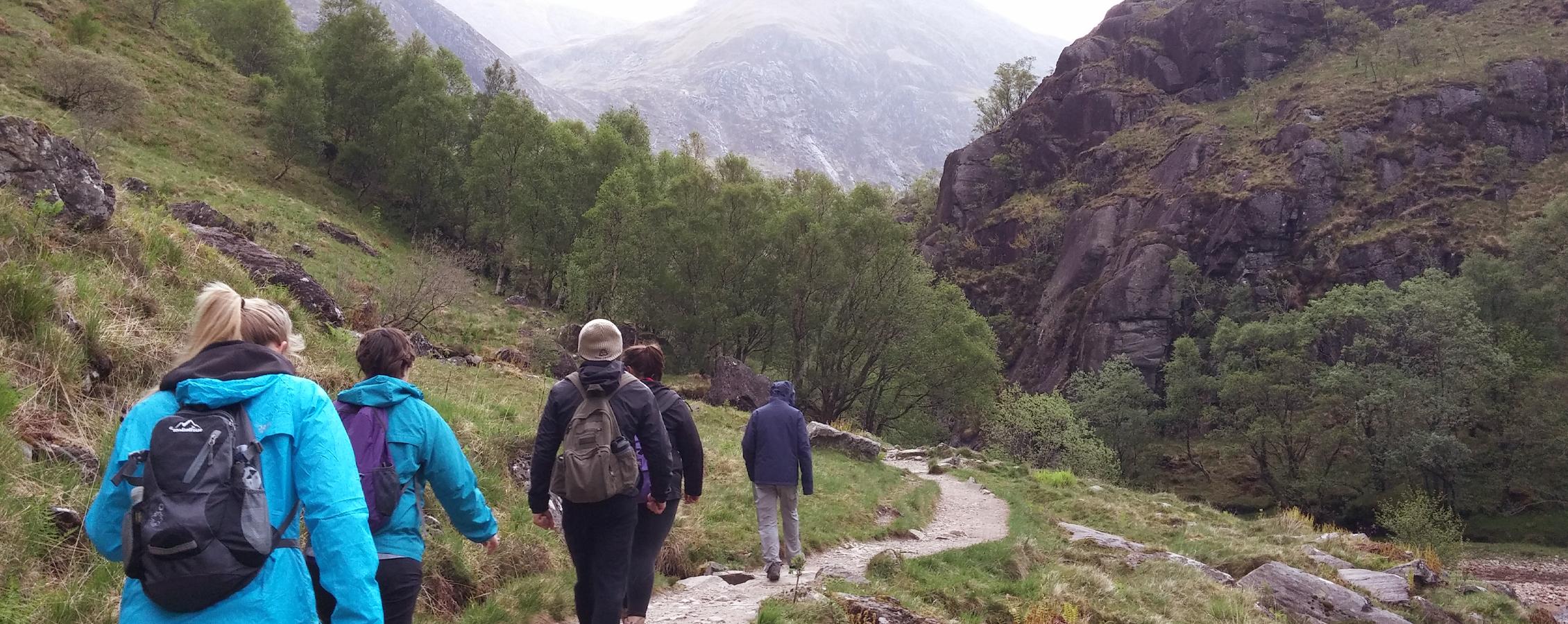 A group of people hike on a worn path amidst mountains and clouds.