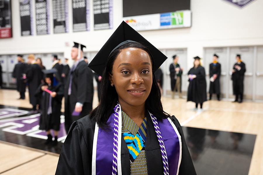 An international student is dressed in academic regalia and smiles at the camera.